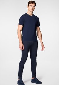 Granatowa koszulka z krótkim rękawem zestawiona z granatowymi dżinsami joggerami o dopasowanym kroju. Oba elementy wykonane z miękkiego, teksturowanego materiału. Całość dopełniają czarne sneakersy.