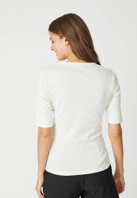 White short-sleeve top in soft fabric with a round neckline. Features a fitted shape and smooth texture, suitable for casual wear.