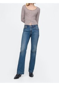 Ljusgrå långärmad topp med rundad halsringning och knäppning; kombinerad med blå utsvängda denimjeans och svarta ankelstövlar.