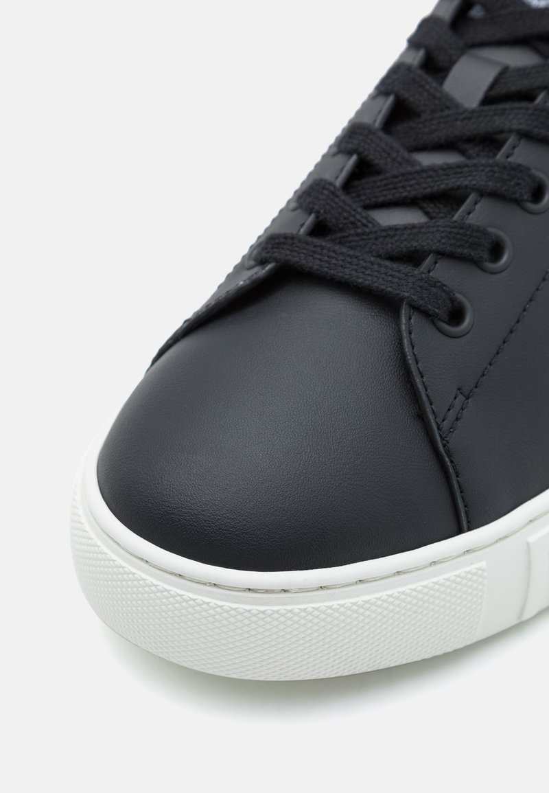 Baskets en cuir noir avec une finition lisse, dotées de lacets noirs, d'un embout arrondi et d'une semelle en caoutchouc blanc texturé.