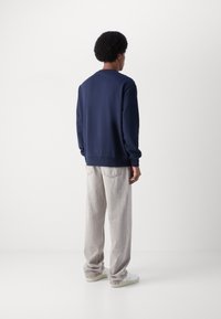 Sudadera navy con un diseño sencillo, cuello redondo y puños de canalé, combinada con jeans sueltos de color gris claro y zapatillas blancas.