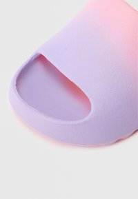 Įsispiriamas sandalų modelis, kuriame naudojamas perėjimas nuo levandų spalvos iki rožinės, pagamintas iš minkštos, tekstūruotos medžiagos, atviru noseliu ir suapvalintais kraštais.