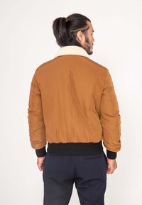 Czarna kurtka bombowca z pluszowym, kremowym kołnierzem, prążkowanymi czarnymi mankietami i dołem oraz pikowanym wzorem, prezentująca dopasowany, casualowy styl.