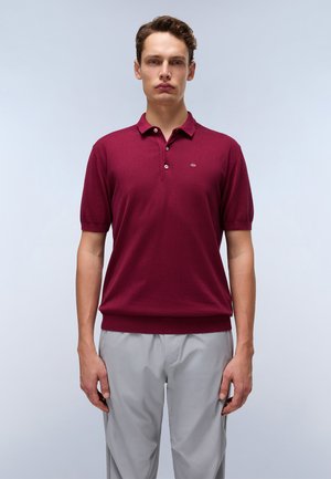 Cămașă polo cu mânecă scurtă de culoare burgundy, cu guler, având trei butoane și un logo subtil pe piept. Material moale din tricot, cu o croială lejera.