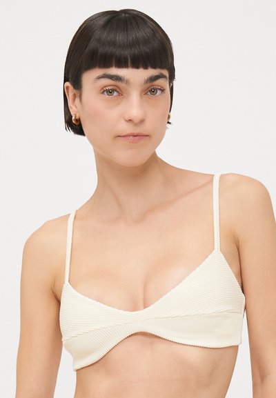 Haut de bikini couleur crème avec une texture côtelée, de forme triangulaire et des bretelles fines réglables. Présente un design ondulé le long des bords.