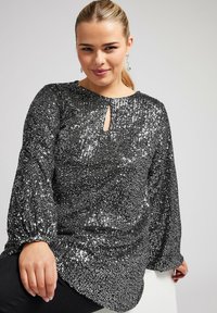 Top nero ricoperto di paillettes con maniche lunghe e voluminose e una scollatura a chiave. Il tessuto è lucido e testurizzato, creando un aspetto straordinario.