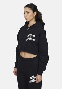 Felpa nera corta con zip frontale, caratterizzata dalla stampa bianca "Good for Nothing". Il materiale è morbido con una vestibilità comoda. Abbinata a pantaloni coordinati.