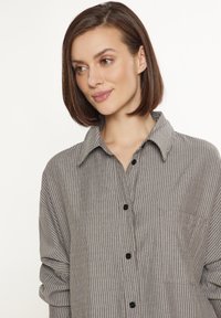 Camicia a righe grigia e bianca con colletto, taschino sul petto, bottoni neri e maniche arrotolate.