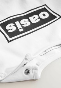 Weißer Baumwoll-Body mit einem großen schwarzen "oasis"-Logo auf einem rechteckigen Patch. Enthält Druckknöpfe am Boden für einfaches Wechseln.