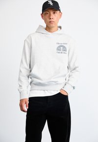 Grijze hoodie met een voorzak, voorzien van een zwarte grafische print op de borst. Gepaarde met zwarte corduroy broek.