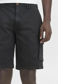 Bermudas negras con cierre de botón, bolsillos laterales, corte entallado y tejido ligero. Presenta costuras visibles y un acabado suave.