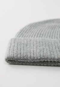 Γκρι πλεκτό σκουφί με ριγέ υφή. Η μπάλλα είναι διπλωμένη, αποκαλύπτοντας μια μαλακή, χοντρή κλωστή που φαίνεται ζεστή και άνετη.