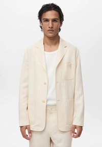 Lyse beige blazer med skråkrave, to forlommer og lyse knapper. Bæres over en hvid T-shirt med rund hals, glat tekstur.
