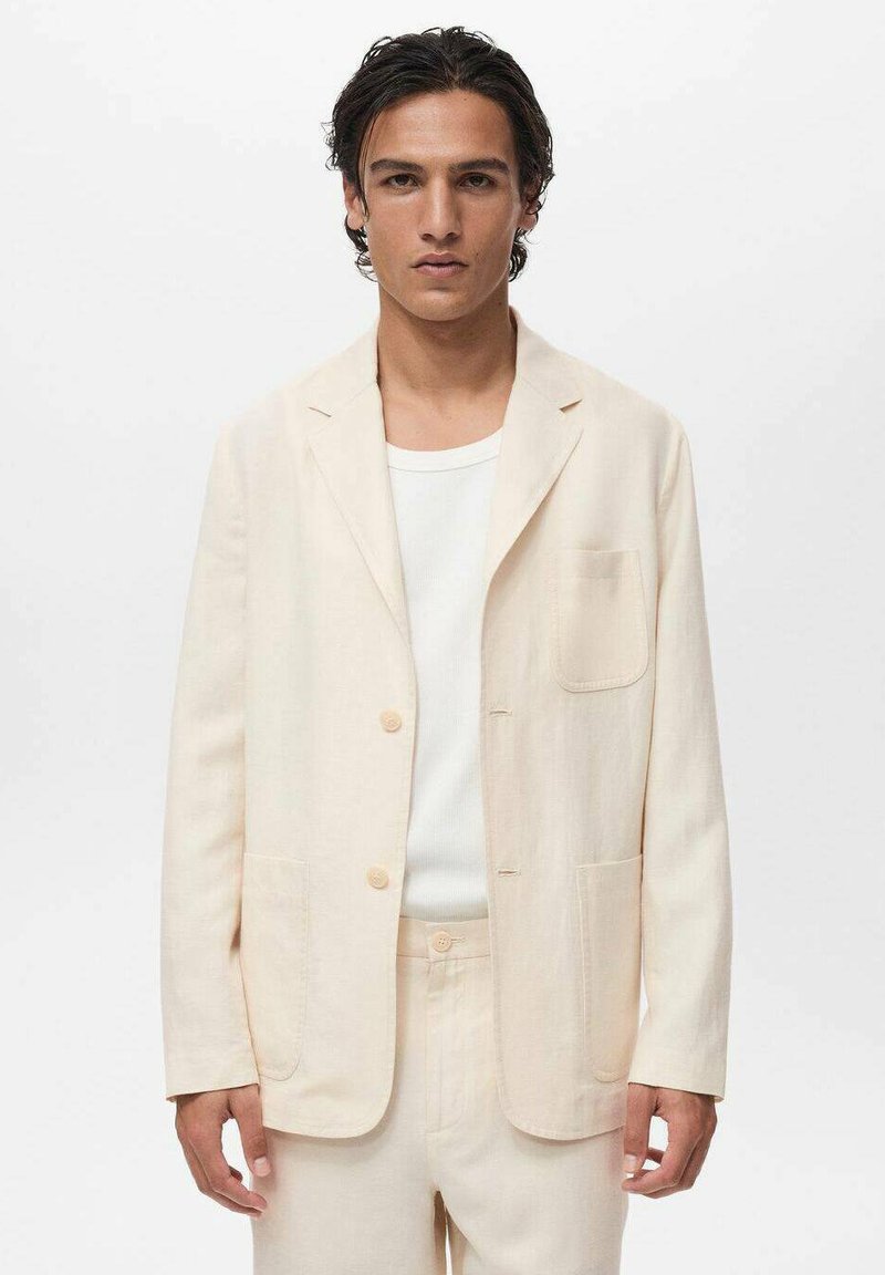 Lyse beige blazer med skråkrave, to forlommer og lyse knapper. Bæres over en hvid T-shirt med rund hals, glat tekstur.