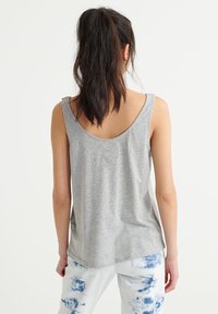 Canotta grigia senza maniche con scollo arrotondato e vestibilità comoda, abbinata a pantaloni azzurri tie-dye. Tessuto dalla superficie liscia.