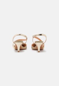 Sandales dorées à lanières avec un petit talon, avec une finition métallique et des brides de cheville texturées. Design ouvert à l'avant avec un intérieur lisse.