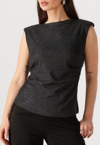 Zwart mouwloos topje met een subtiele glittertextuur, een ronde halslijn en een losse pasvorm. Geaccentueerd met zachte schouderdetails.