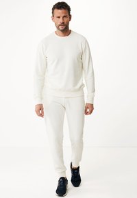 Krämfärgad sweatshirt och matchande joggers, båda gjorda av mjukt tyg, med klassisk passform och ribbade muddar, parat med svarta sneakers.