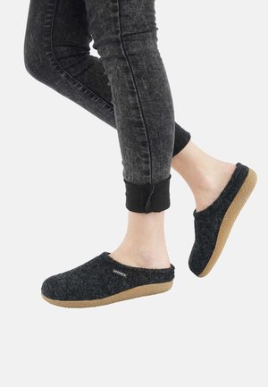Grey felt slip-on shoes with a textured surface, cork outsole, and minimal branding, paired with black tapered jeans at ankle height.