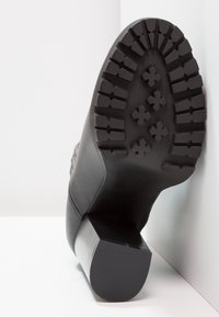 Czarne botki za kostkę z teksturowaną skórzaną cholewką, kwadratowym obcasem i gumową podeszwą z bieżnikiem w formie wypukłych krzyży i rowków.