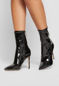 Czarne lakierowane botki za kostkę z wąskimi noskami i wysokimi obcasami w kształcie szpilki. Posiadają zamek błyskawiczny oraz marszczony design na cholewce.
