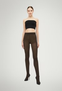 Brune uigennemsigtige strømpebukser med en glat tekstur, høj talje og en tætsiddende pasform, kombineret med en sort bandeau-top og højhælede sko.