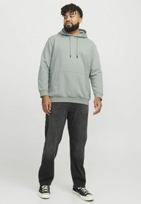 Grå hættetrøje med lomme foran, parret med mørke jeans og sorte sneakers. Har snore og en afslappet pasform.