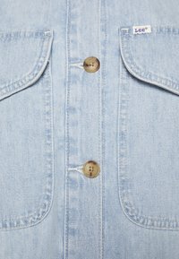 Jasnoniebieska koszula denimowa z dwoma kieszeniami na piersi, z brązowymi guzikami i białymi przeszyciami. Logo Lee na prawym ramieniu.