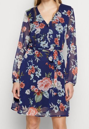 Tummansininen kukkakuvioinen mekko, jossa on pitkät läpikuultavat hihat, V-aukko, nappikiinnitys edessä ja vyötäröllä solmittava saman värinen kangasvyö.