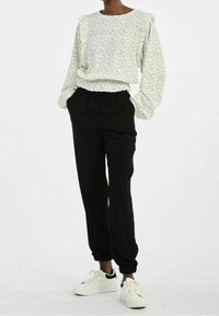 Witte lange mouw top met zwarte stippen en ruffles op de schouders, gecombineerd met zwarte joggerpants en witte sneakers.