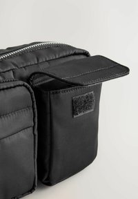 Borsa in tessuto nero con chiusura a zip, caratterizzata da un design testurizzato e imbottito e un flap in velcro per ulteriore spazio di archiviazione o chiusura.