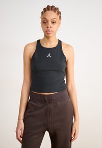 Črn kratki top s racerback obliko, ki ima spredaj bel Jumpman logo. Dopolnjen z temno rjavimi flis jogger hlačami.