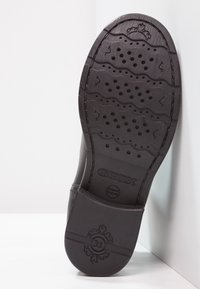 Suela de un zapato Geox negro con dibujo en la suela, agujeros de ventilación y el tamaño "31" grabado en el talón, sobre un fondo blanco.