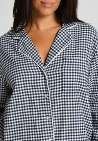 Navy en witte gingham patroon pyjama top, met een kraag, zak, knoopsluiting en witte bies langs de randen.