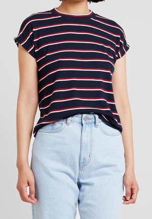 Camiseta de manga corta a rayas en azul marino con líneas horizontales rojas y blancas. Textura acanalada, cuello redondo, ajuste relajado. Combinada con jeans de color azul claro.