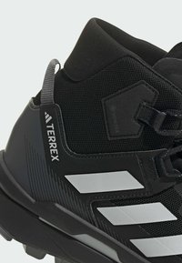 Czarne buty trekkingowe z teksturowaną siateczką, gumową podeszwą, odblaskowymi białymi akcentami oraz etykietą GORE-TEX po boku.