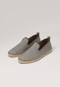 Espadrilles de diseño slip-on con un upper de tela a cuadros en blanco y negro, forro textil marrón, suela clásica de yute y lengüetas de tira.