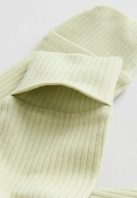 Vaaleanvihreät, ribbineulotut sukat taitetuilla varresuilla, esillä valkoisella alustalla korostaen tekstuuria ja kangasdetailia.