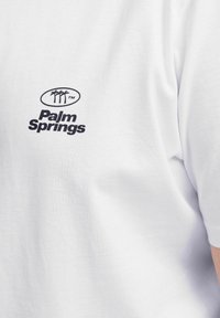 Hvid bomulds T-shirt med et sort logo med palmer og teksten "Palm Springs", korte ærmer og en afslappet pasform.