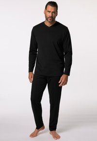 Zwarte lange mouw V-hals top gecombineerd met zwarte gestreepte broek, beide gemaakt van een zachte, gladde stof. Blootsvoets staan op een neutrale achtergrond.