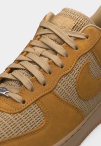 Gros plan sur une chaussure de sport beige clair et beige avec un tissu texturé et des panneaux en daim, des lacets beiges et un logo Nike swoosh cousu sur le côté.