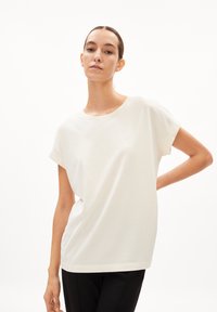 T-shirt crème à manches courtes avec un col rond, coupe ample et petit logo sur la poitrine gauche. En coton, texture lisse.