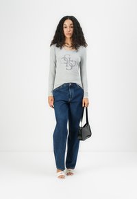 Hallide volti-sleeve shirt, millekujutus, sinised kõrge vööjoonega teksad, valged avatud varvastega sandaalid ja must käekott.