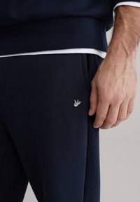 Donje hlače tamnoplave boje od mešavine mekane pamuka, s rebrastim pojasom, bočnim džepovima i malim bijelim izvezenim logotipom na lijevom boku.