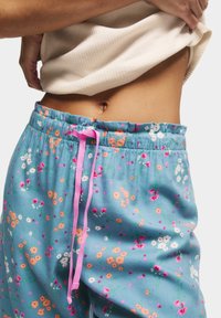 Blå blommiga pyjamasbyxor med en rosa dragsko, tillverkade av ett mjukt och lätt tyg med en rynkad midja och färgglada blommönster.