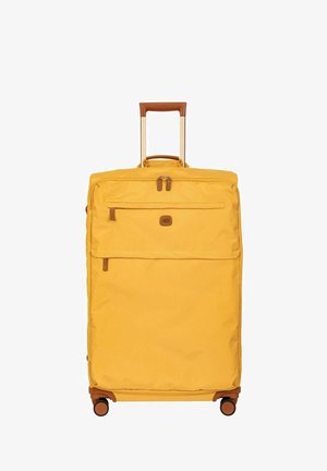 Valise souple jaune avec poignée marron, poches zippées à l'avant et quatre roulettes pivotantes, debout avec poignée télescopique étendue.