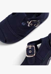 Navy canvas sandals with an open toe and buckle detail. Features contrasting stitching, adjustable strap, and textured sole for grip.