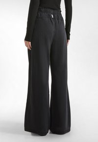Pantaloni in denim neri a gamba larga con fascia smock, caratterizzati da una texture liscia, un design casual e una finitura dell'orlo discreta.