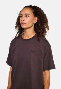 Ciemnobrązowa, oversize t-shirt wykonana z bawełny, z krótkimi rękawami i małym haftem "HALO" na klatce piersiowej. Gładka faktura.