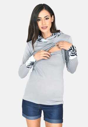 Graues Langarmoberteil mit Kapuze und gemusterten Bündchen, mit einer Öffnung zum Stillen. Kombiniert mit Jeansshorts und einem lässigen Stil.